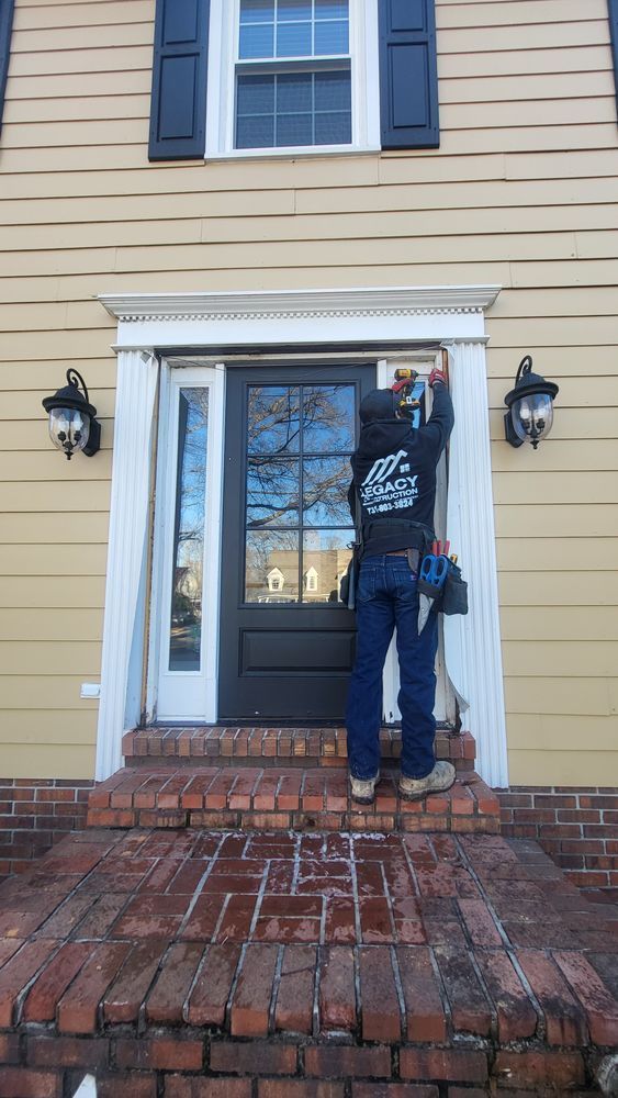 Person installing trim around a black front door on a yellow house with brick steps.