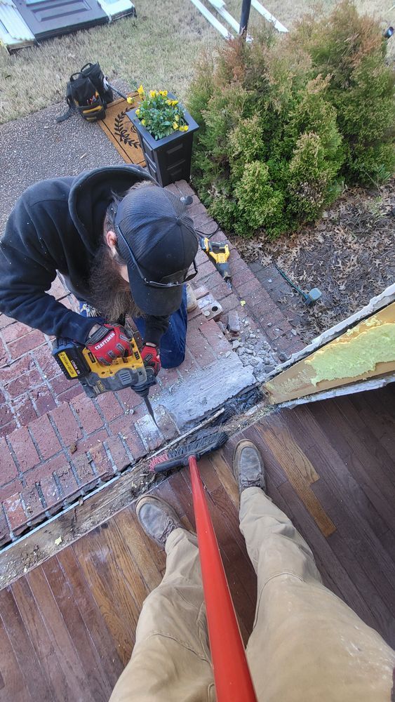 Person kneeling, using a drill on brick steps, next to a door frame.
