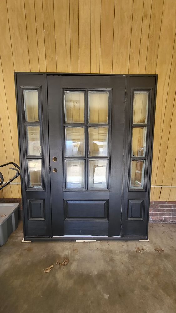 Black front door with sidelights, set against wooden wall.