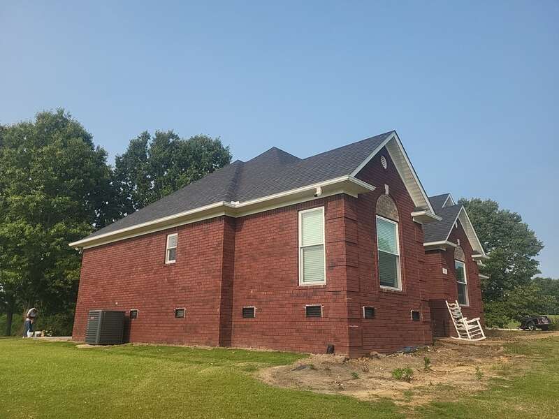 Red brick house with dark roof and white trim under a blue sky.