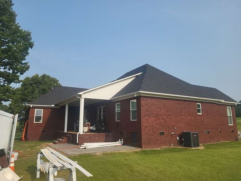 Red brick house with a dark roof and white trim under a clear blue sky.