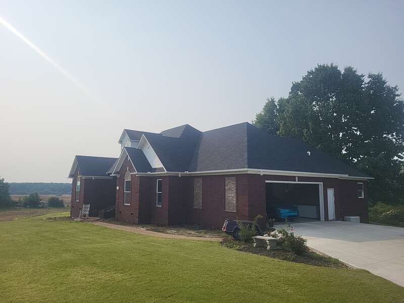 Red brick house with a dark roof and an open garage door, set on a green lawn.