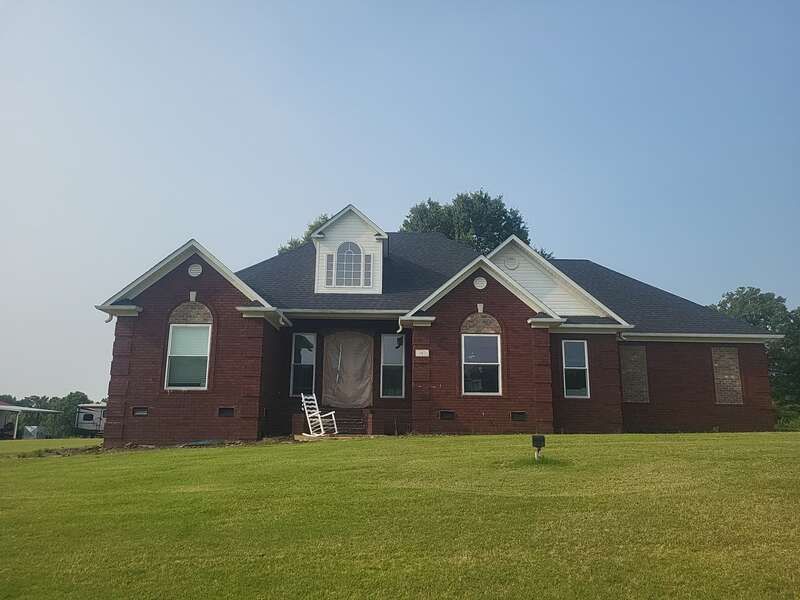 Red brick house with boarded windows, green lawn, clear sky.