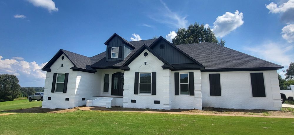 White house with black trim and roof, green lawn, blue sky with clouds.