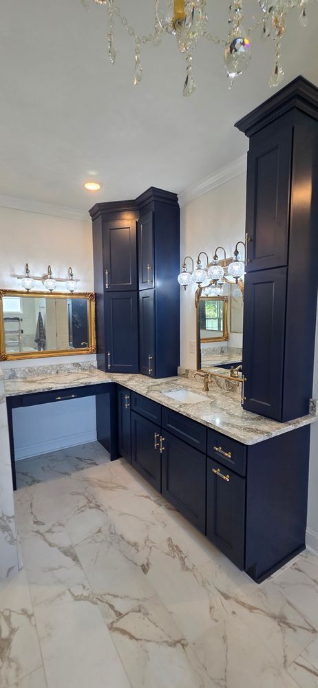 Bathroom with dark blue cabinets, marble countertops, mirrors, and chandelier.