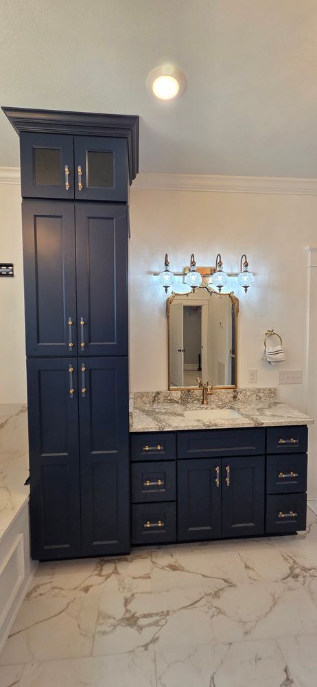 Navy blue bathroom vanity with tall storage cabinet, marble countertop, and a decorative light fixture.