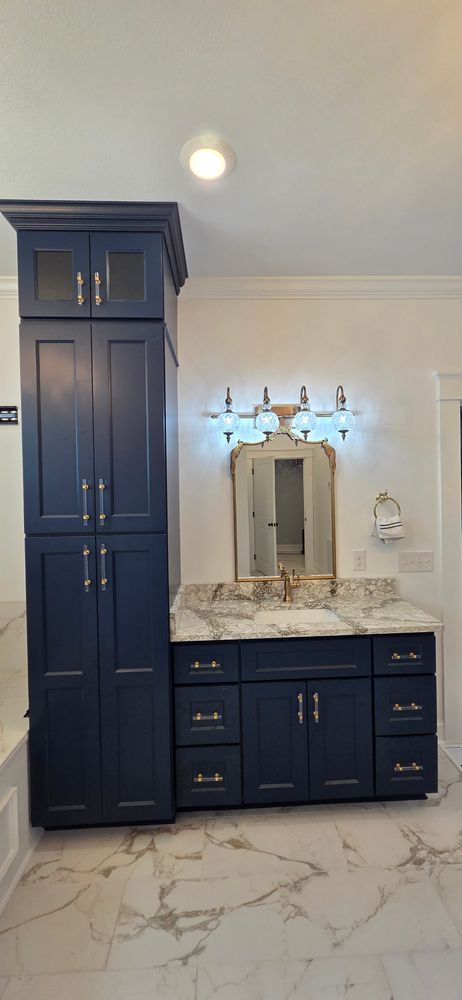 Navy blue bathroom vanity with tall cabinet, marble countertop and flooring, and decorative mirror.