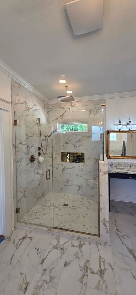 Marble-tiled shower with glass doors and a brushed bronze showerhead.