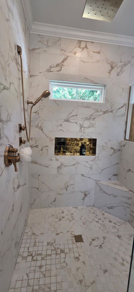 Shower with white marble tiles, golden fixtures, and a window.
