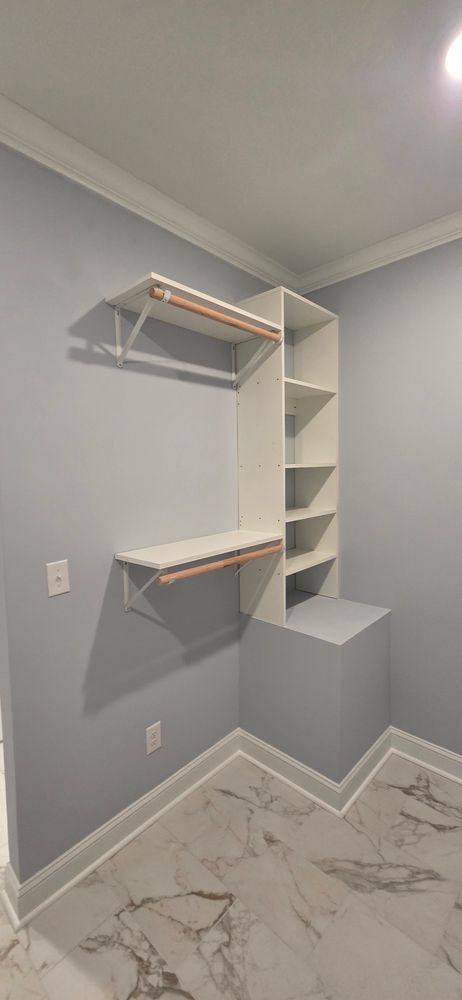 A white closet organizer in a corner of a room with light blue walls and marble flooring.