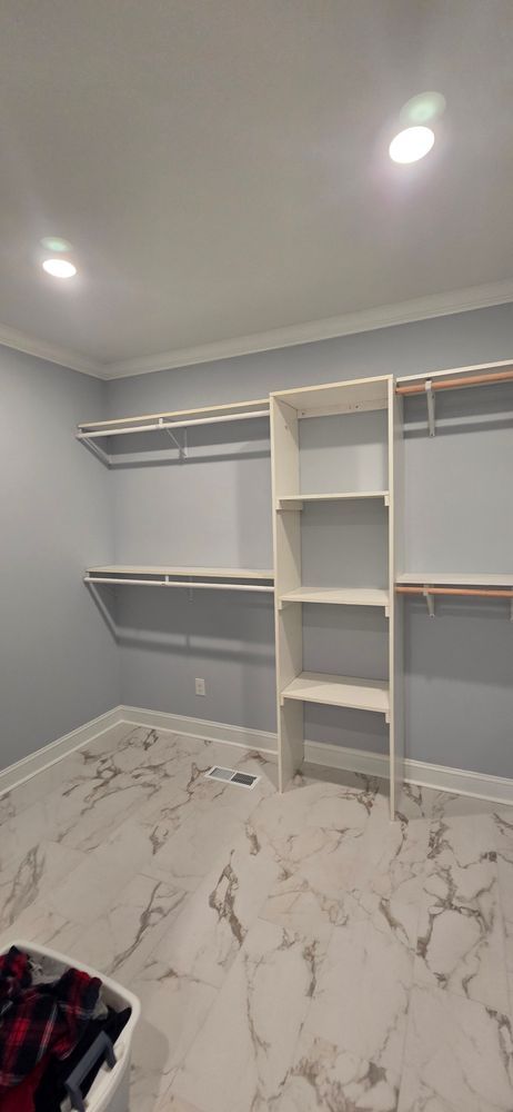 Empty walk-in closet with shelves, rods, and marble-look flooring. Pale blue walls, white trim and ceiling.