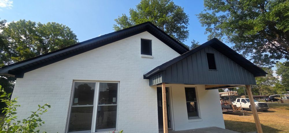 White house with a dark roof and porch, surrounded by trees.