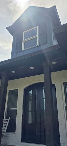 Exterior view of a house with a dark blue upper story and black trim. A dark front door is centered under a covered porch.