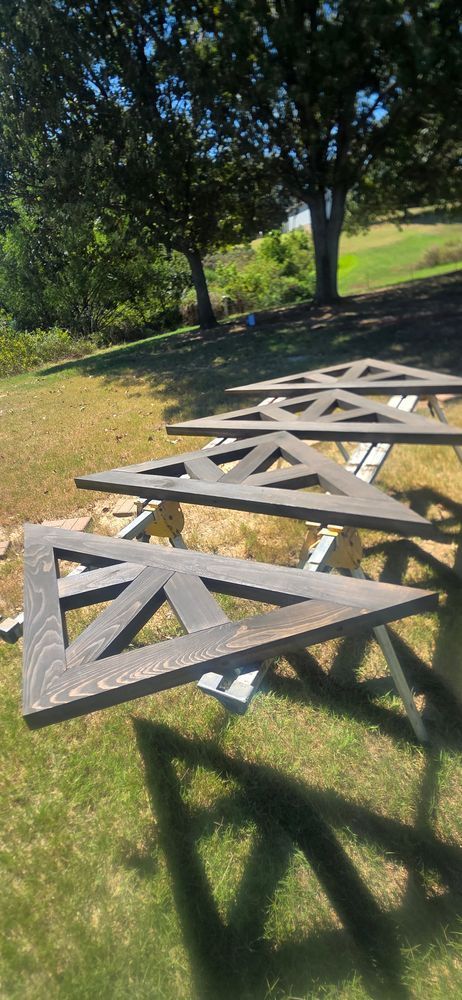 Triangular wooden structures resting on saw horses outdoors. Green grass and trees are in the background.