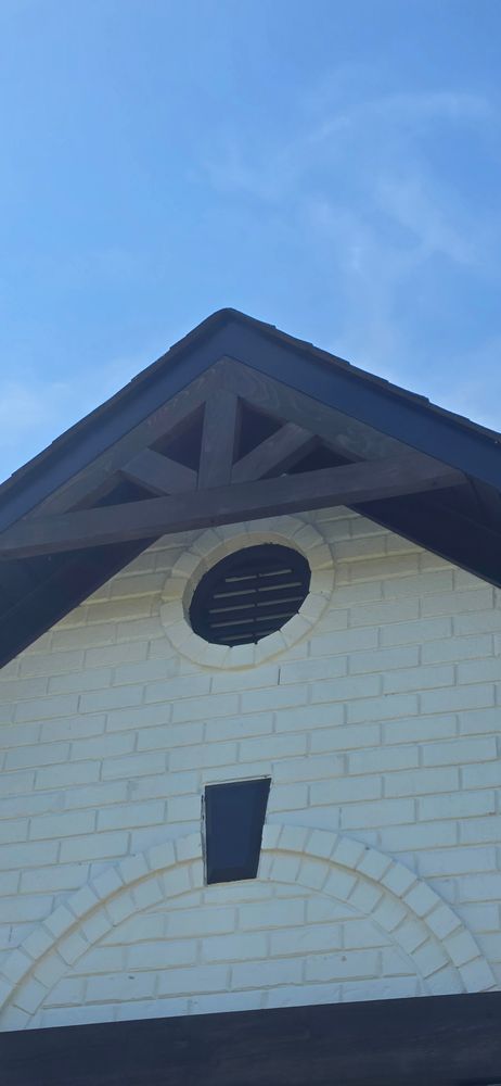 White brick building with a dark roof and decorative wooden beams against a blue sky.