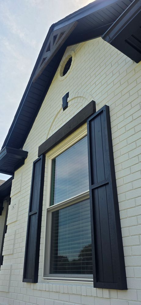 Exterior view of a white brick house with black shutters, trim, and roof. A window is in the center.