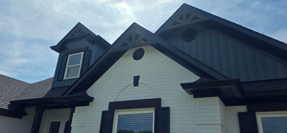 Close-up of a house with white brick walls and dark blue siding. The roof has black trim and decorative woodwork.