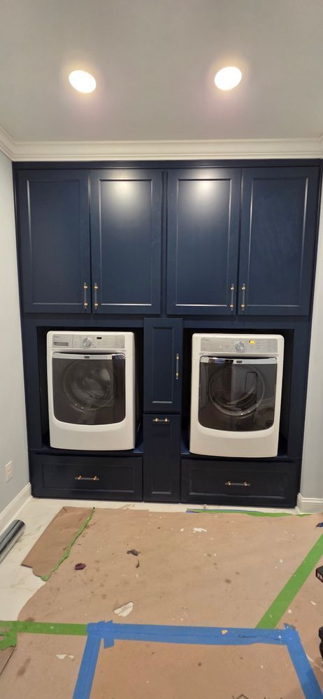 Laundry room with built-in dark blue cabinets, washer and dryer. Cardboard and tape on the floor.