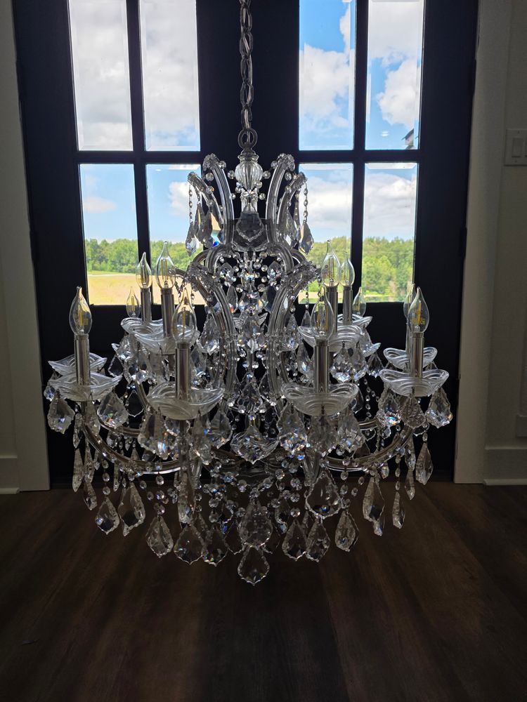 Crystal chandelier hanging in front of a window overlooking a field and sky.