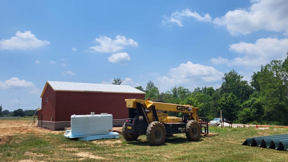 Red barn and yellow forklift on a construction site under a blue sky with clouds.