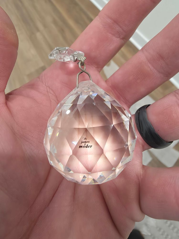 Person's hand holding a faceted crystal pendant with a small logo and metal hardware.