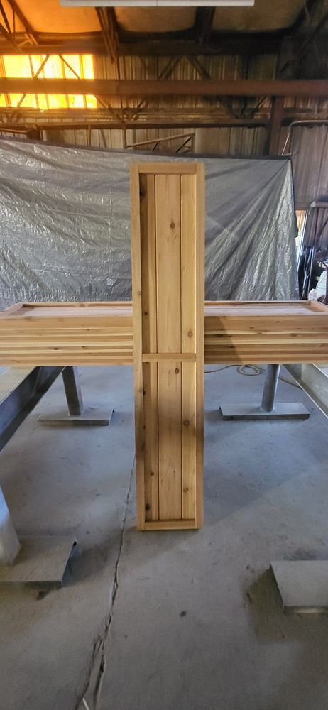 Wooden cabinet in a workshop. Light wood cabinet standing upright on concrete floor. Background is a tarp and wood.
