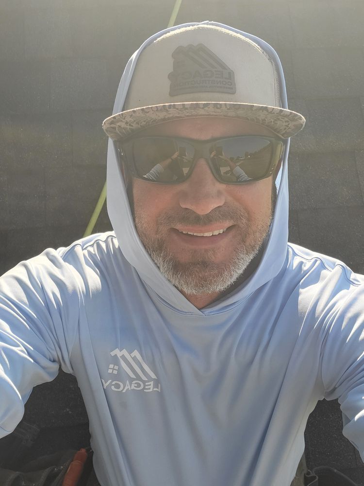 Man wearing sunglasses, hat, and hoodie, smiling in bright sunlight.