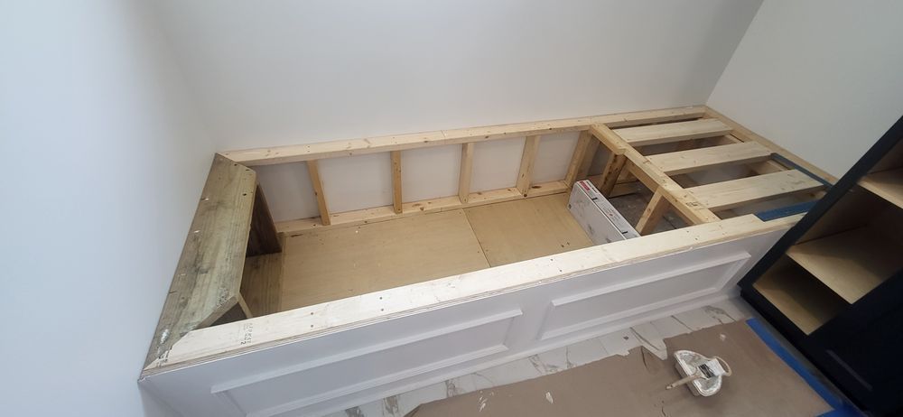 Wooden frame construction of a built-in bench in a white room.