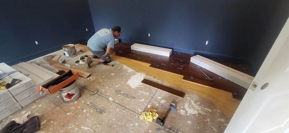 A person installing a dark wood floor in a room with blue walls, tools and materials scattered around.