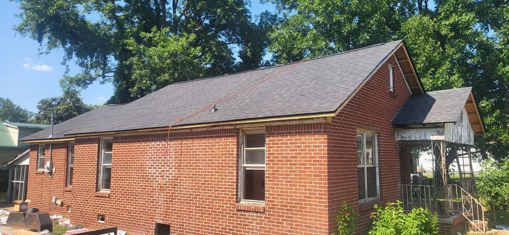 Brick house with a dark roof and green trees in the background.