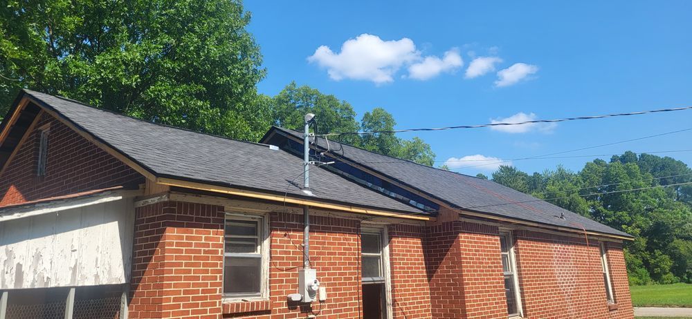 Brick house with dark gray roof against a blue sky with trees.