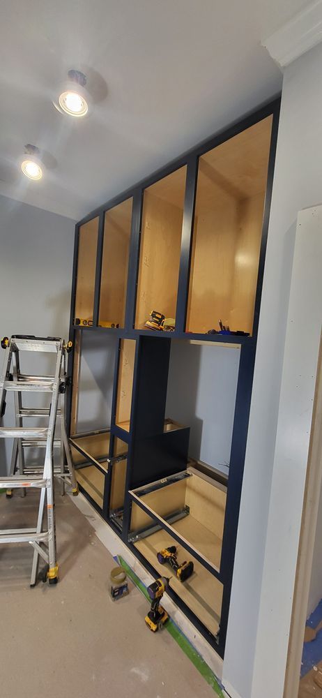 Cabinetry installation in a room, featuring upper and lower cabinets with dark trim and wood interiors.