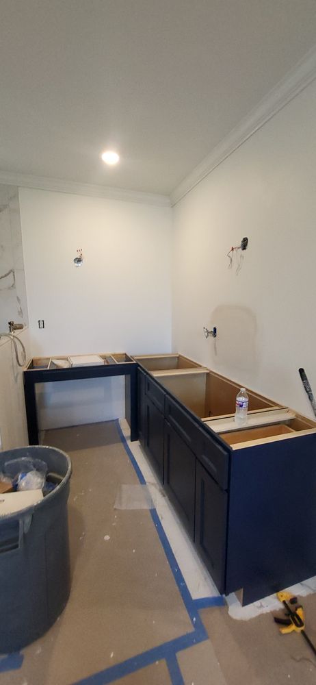Kitchen cabinets under construction, navy blue cabinets against white walls, blue tape on floor.