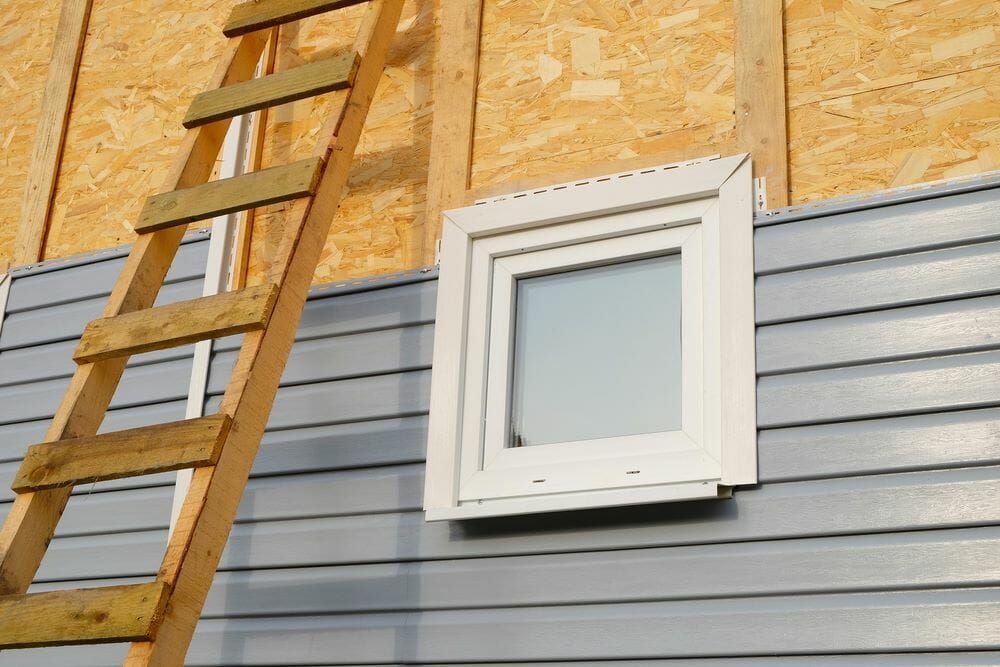 A worker wearing gloves is installing siding on the exterior of a house.