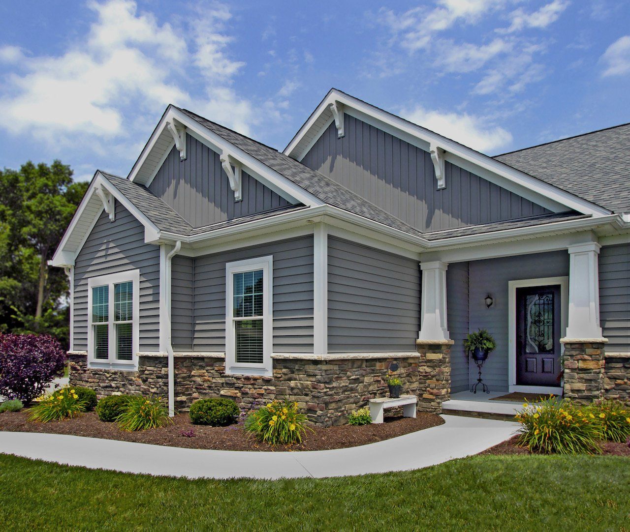 Gray house with white trim, stone base, and green lawn under a blue sky.