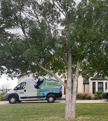 A service van parked on a front lawn in front of a house. A tree stands in the foreground.