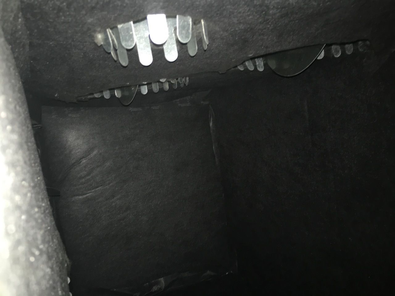 Dark, interior view, possibly inside a vehicle. Metal vents are visible against a black, textured surface.