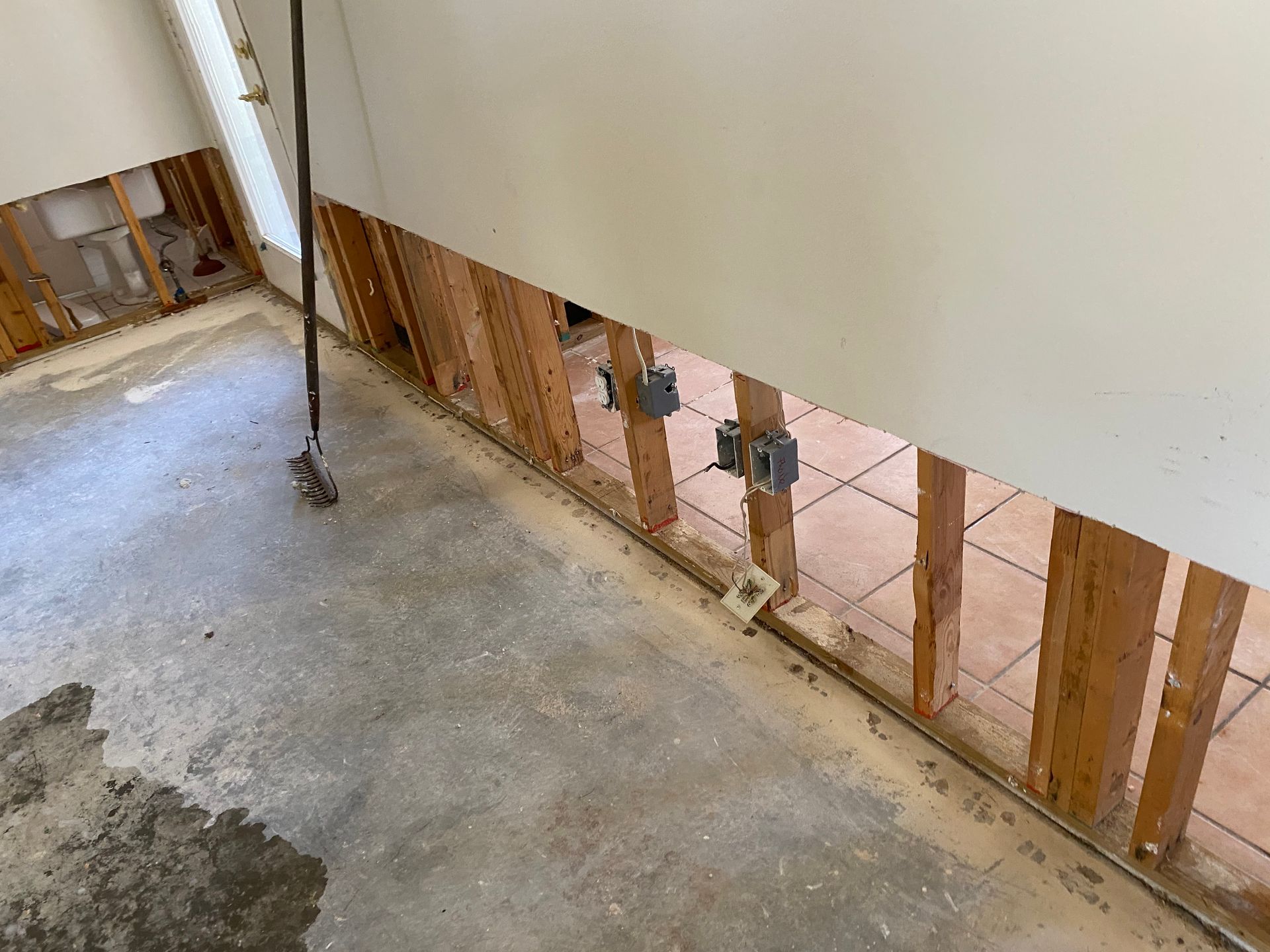 Interior wall damage, revealing studs and electrical boxes. Concrete floor with debris.
