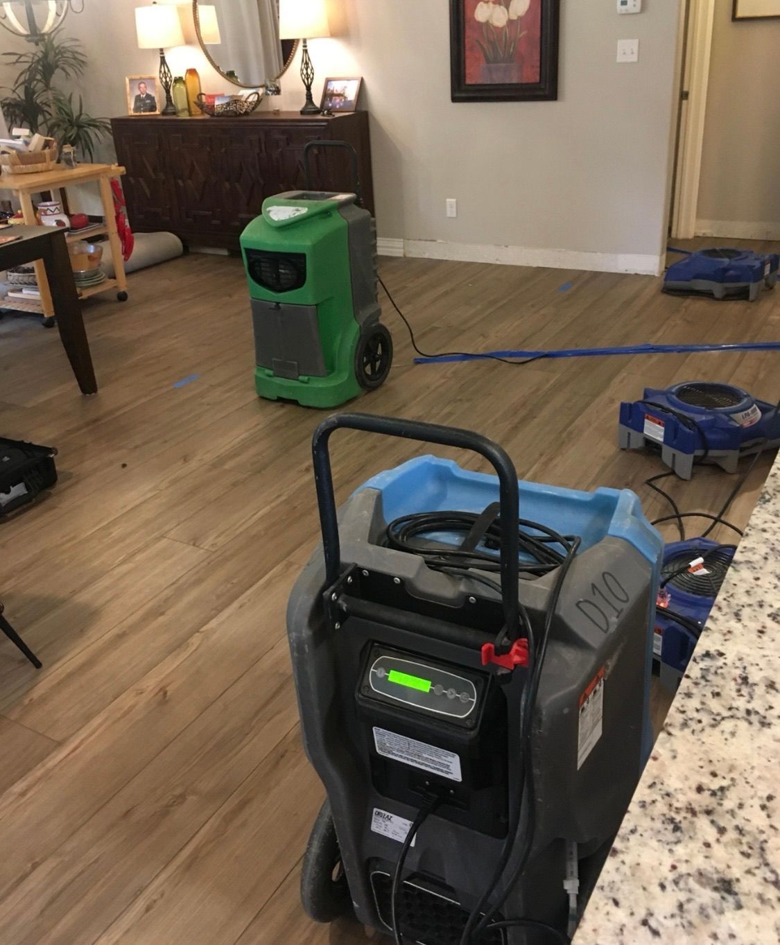 Dehumidifiers and air movers in a home, likely for water damage restoration. One green and one gray machine are visible.