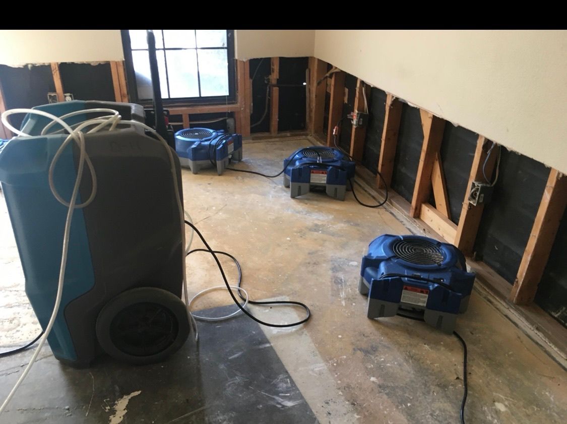 Dehumidifiers in a room with exposed wall studs, likely due to water damage. The machines are blue and gray.