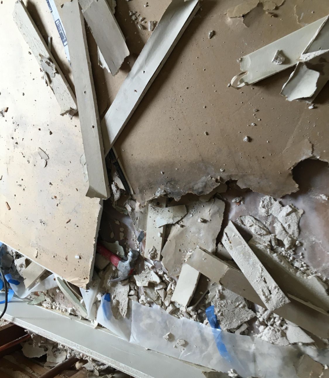 Damaged drywall on a wall, with large pieces broken and scattered, exposing wiring and a hollow space.