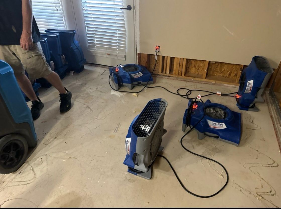 Dehumidifiers drying a room with exposed wall studs and a person walking near a window.