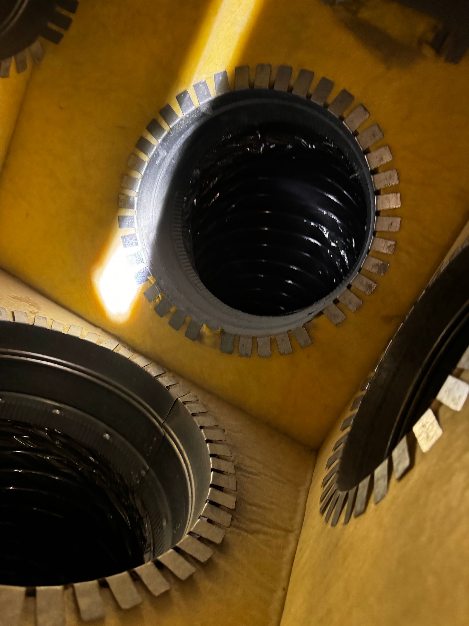 Three circular openings, edged with notched metal, show dark interiors with swirling texture, set in a yellow surface.
