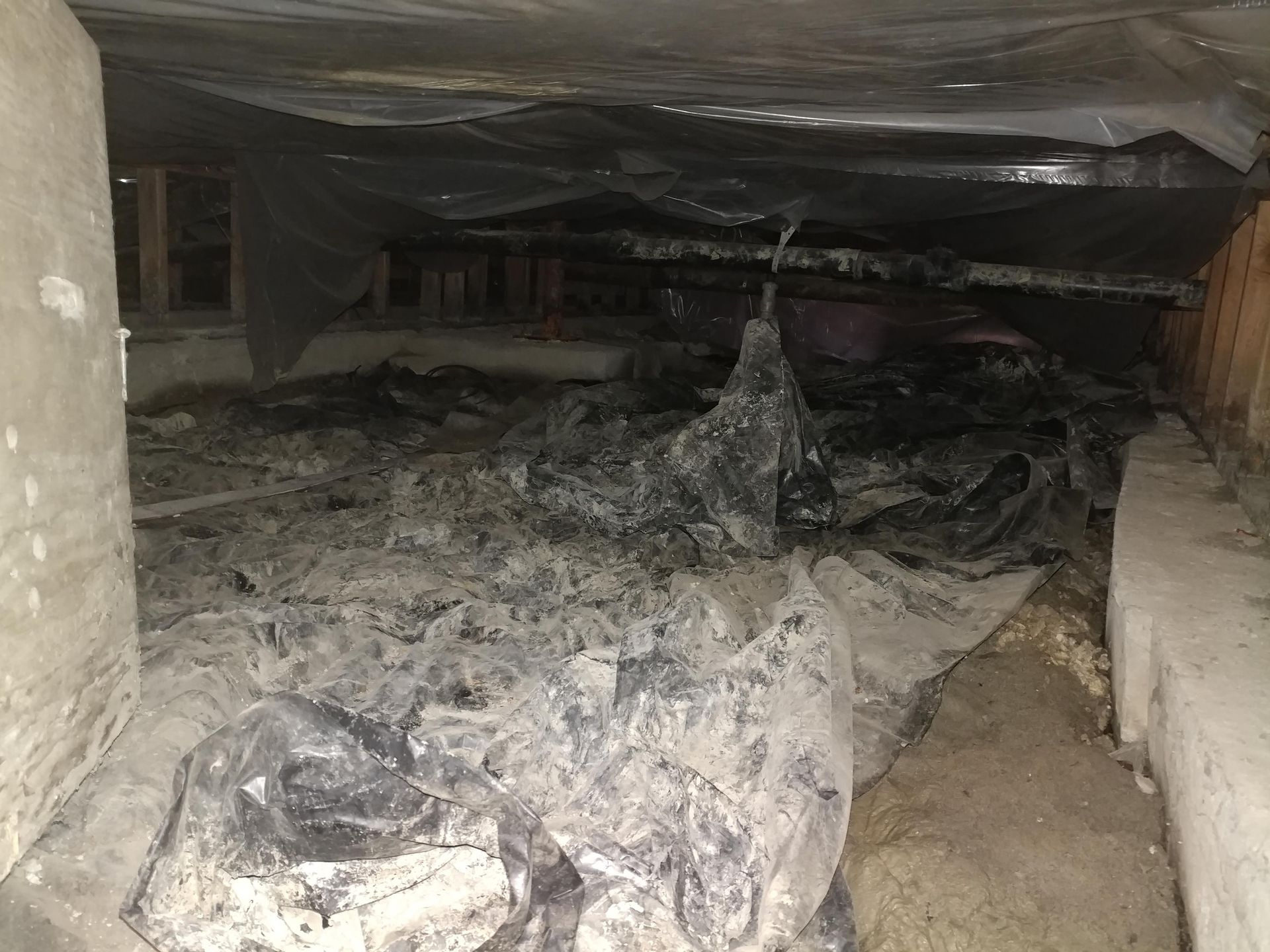 Dark crawl space with black plastic sheeting, dirt, and concrete walls.