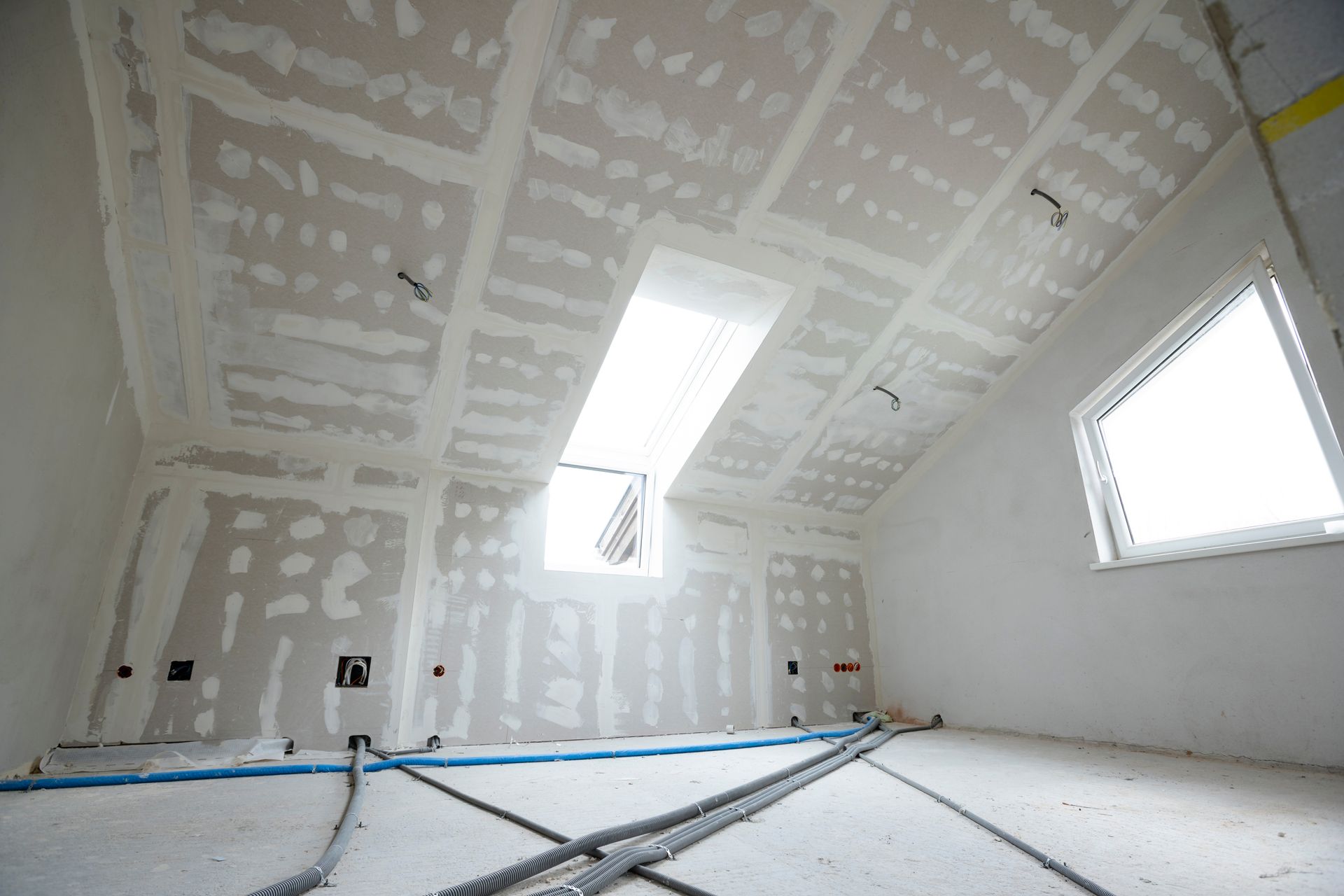 Interior of a room under construction, with drywall partially installed on walls and ceiling, visible windows.