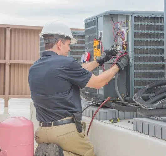 HVAC technician in hard hat repairs rooftop air conditioning unit.