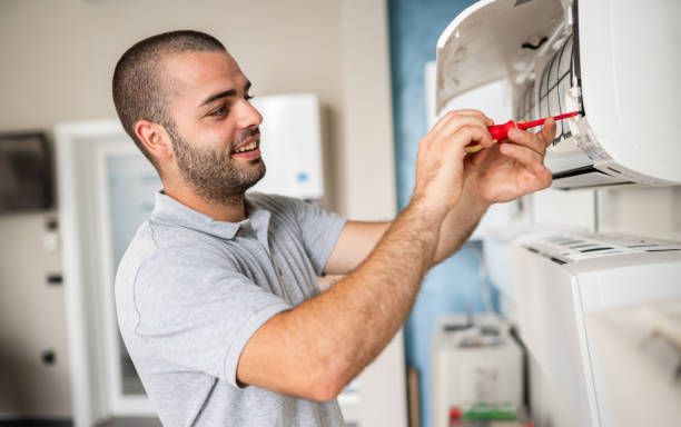 HVAC technician uses a screwdriver to repair an air conditioning unit.