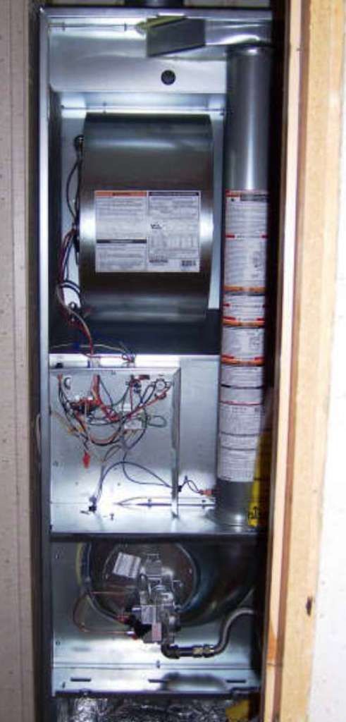 Furnace unit inside a metal cabinet, visible wiring, circular blower, exhaust pipe.