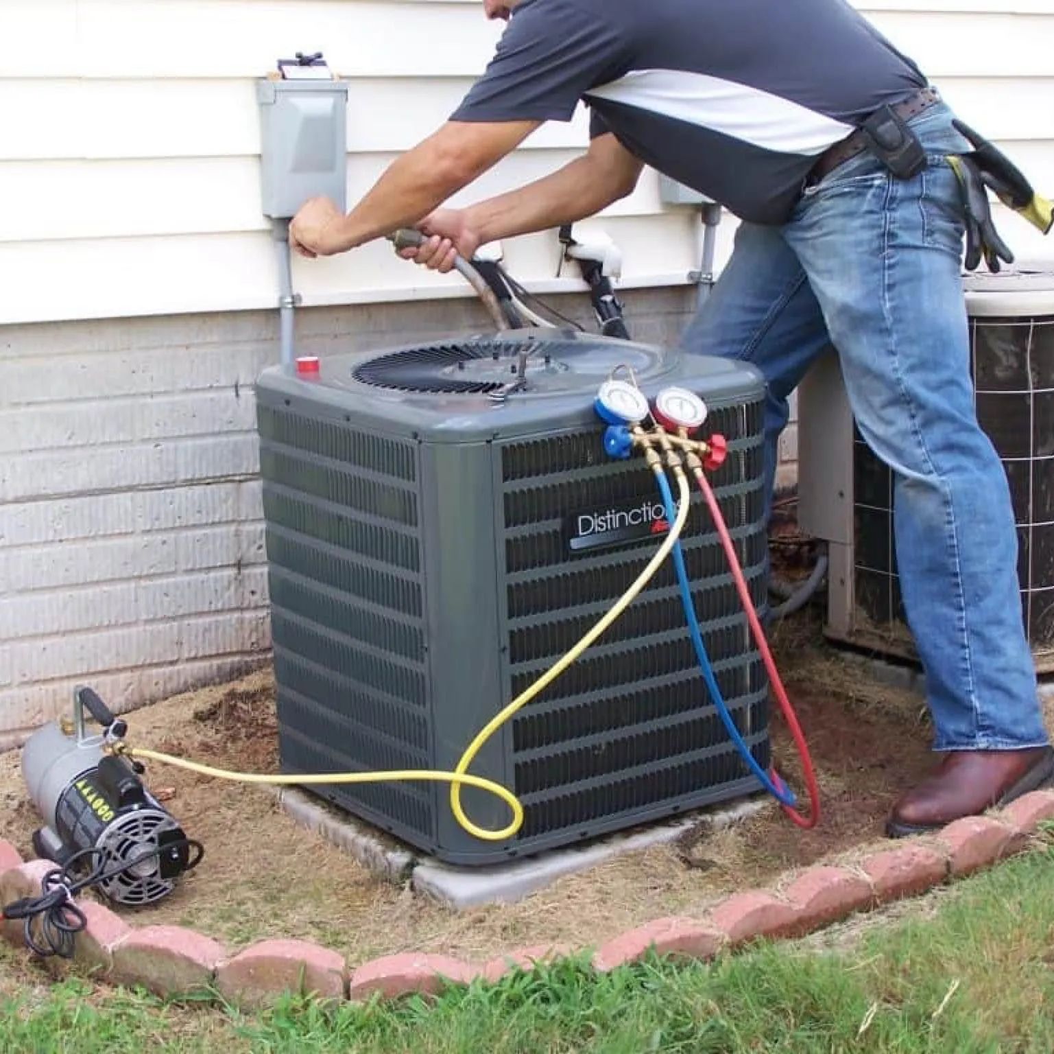 HVAC technician servicing an air conditioning unit outside a house. Hoses connected, tools in hand.