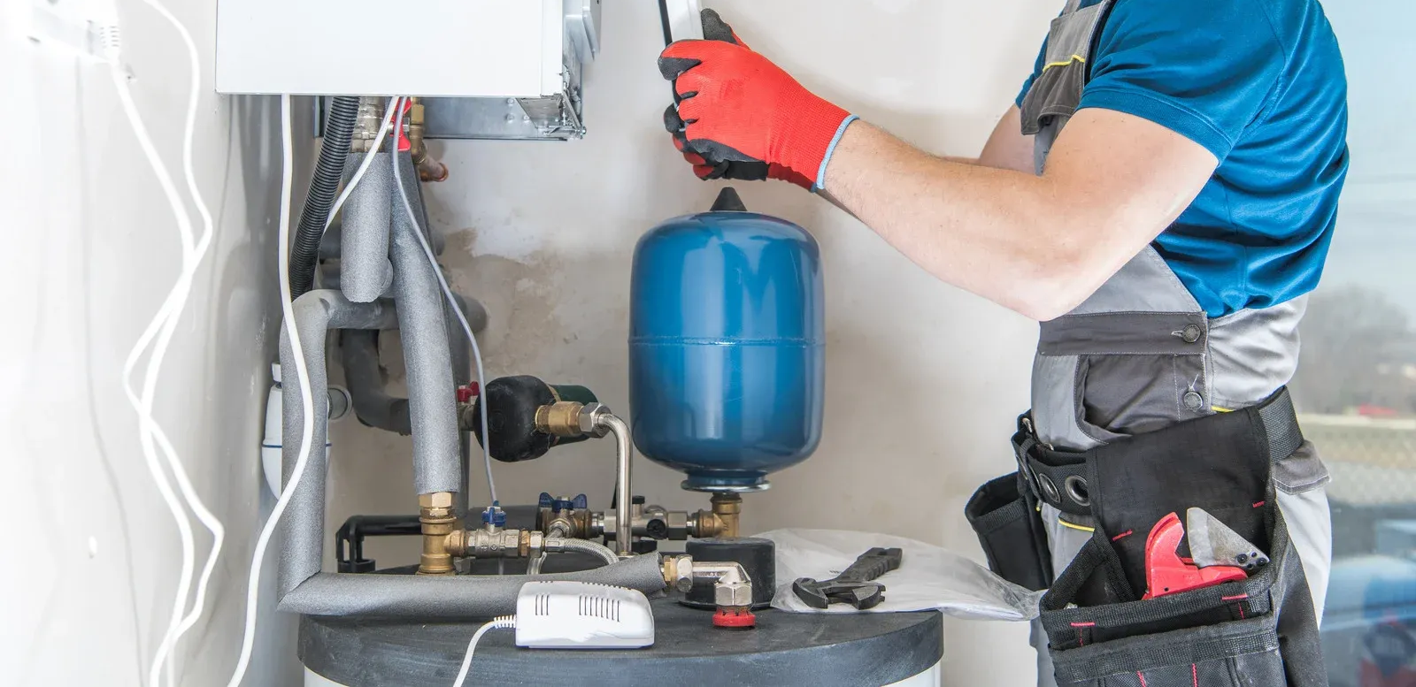 Plumber in red gloves working on water heater components.